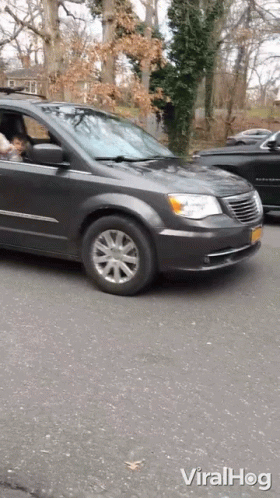 A Gray Chrysler Minivan Is Driving Down The Street GIF