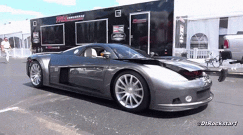 A Gray Sports Car Is Parked In Front Of A Trailer That Says Dtrockstar1 On It GIF