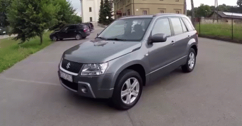 A Gray Suzuki Suv Is Parked In A Parking Lot With Other Cars GIF