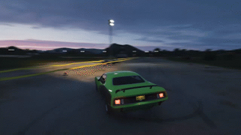 A Green Car Is Driving Down A Road With A Sunset In The Background GIF