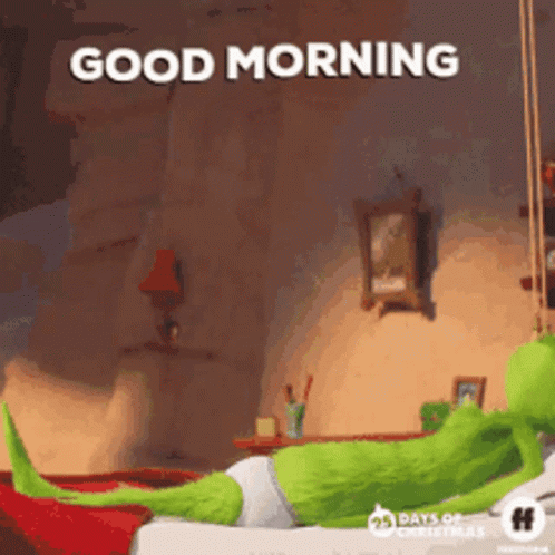 A Green Cartoon Character Is Laying On A Bed With The Words `` Good Morning '' Written Above Him . GIF