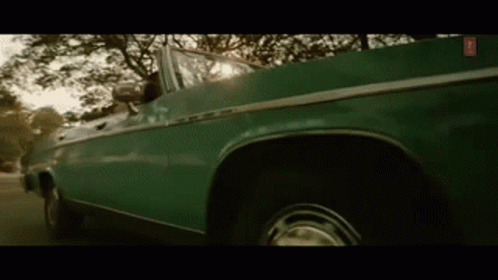 A Green Convertible Car Is Driving Down A Street . GIF