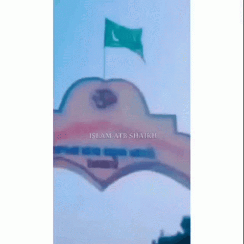 A Green Flag Is Flying In The Wind Over A Building GIF