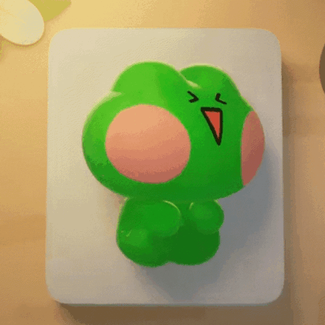 A Green Frog With A Red Beak Is Sitting On A Table GIF