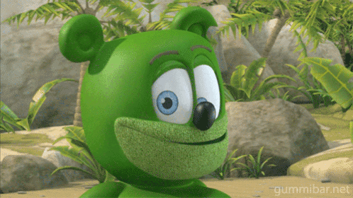 A Green Gummy Bear With Blue Eyes Is Smiling In A Jungle GIF