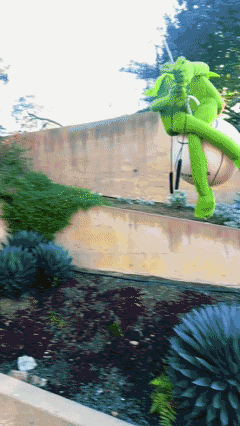 A Green Inflatable Elephant Is Sitting On A Concrete Wall GIF