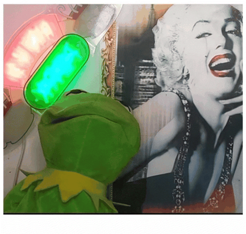 A Green Kermit Frog Is Standing In Front Of A Picture Of Marilyn Monroe GIF