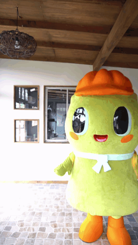 A Green Mascot Wearing An Orange Hat And Orange Feet GIF