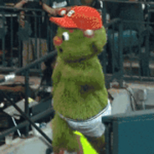 A Green Stuffed Animal Wearing A Red Hat And Diapers GIF