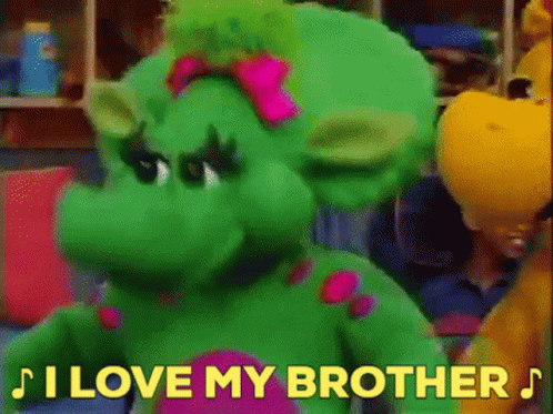 A Green Stuffed Animal With A Pink Bow On Its Head Is Standing Next To A Yellow Stuffed Animal . GIF