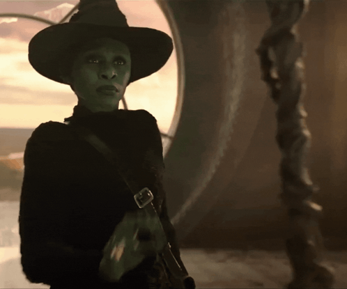 A Green Witch With A Black Hat And A Black Sweater GIF