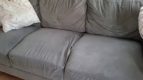 A Grey Leather Couch With White Pillows On It GIF