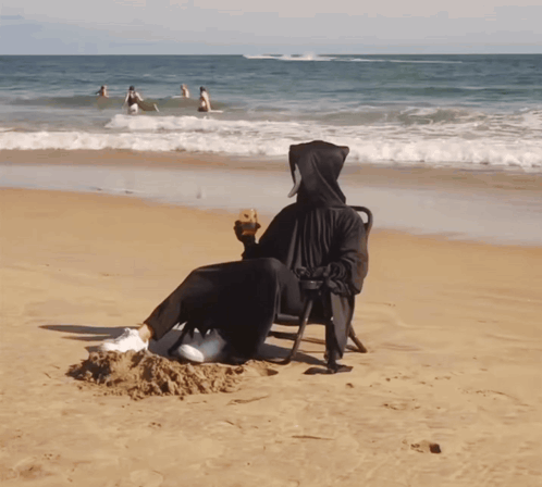 A Grim Reaper Sits On A Beach Holding A Drink GIF