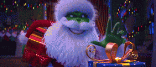 A Grinch Is Holding A Christmas Present And Waving At The Camera . GIF