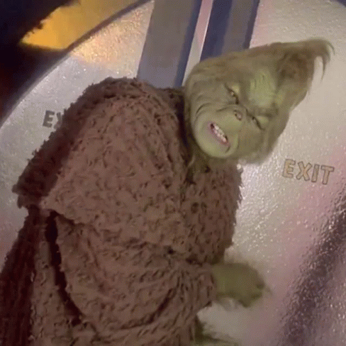A Grinch Is Standing In Front Of A Glass Door That Says Exit GIF