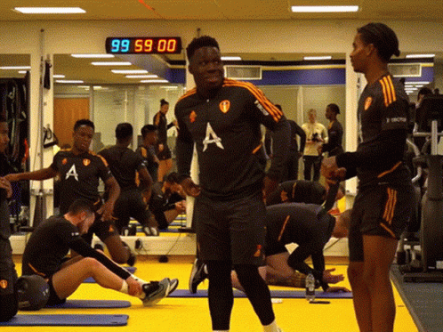 A Group Of Athletes Are In A Gym With A Clock That Says 99 59 00 GIF