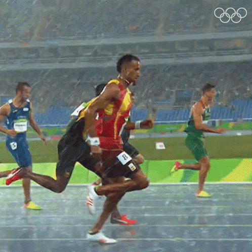 A Group Of Athletes Are Running On A Track With The Olympic Rings Visible In The Background GIF
