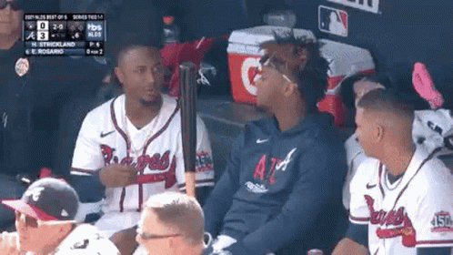 A Group Of Baseball Players Are Sitting In A Dugout With A Bat . GIF