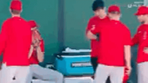 A Group Of Baseball Players Are Standing Around A Blue Cooler On The Field . GIF