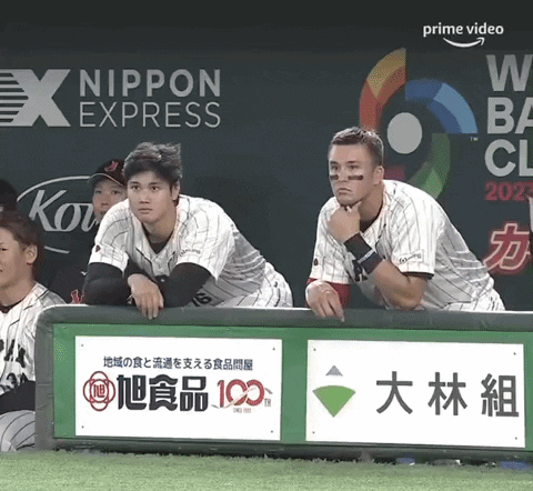 A Group Of Baseball Players Sitting In The Dugout With An Ad For Nippon Express Behind Them GIF