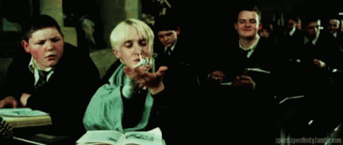 A Group Of Boys Are Sitting At A Table In A Classroom And One Of Them Is Holding A Book . GIF