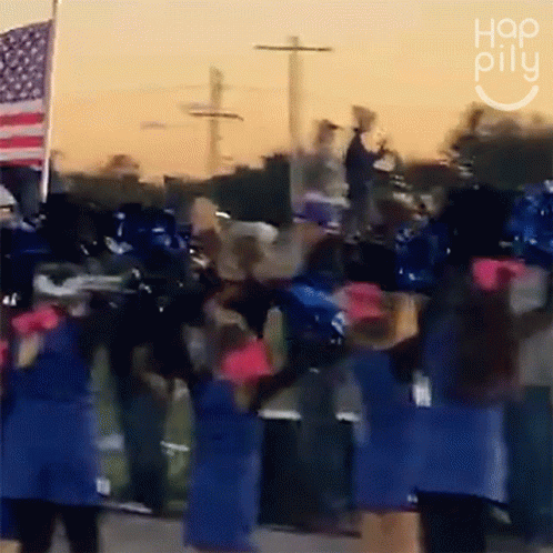 A Group Of Cheerleaders Are Dancing In Front Of An American Flag And A Sign That Says " Hop Pillu " GIF
