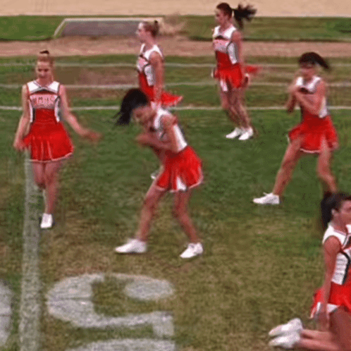 A Group Of Cheerleaders Are Dancing On A Field While Another Cheerleader Sits On The Ground . GIF