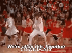 a group of cheerleaders are dancing together on a basketball court while a crowd watches .