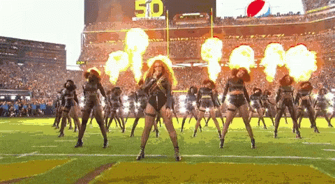 A Group Of Cheerleaders Are Performing On A Football Field In Front Of A Scoreboard With The Number 50 On It GIF