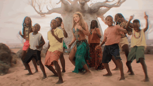 a group of children are dancing in front of a tree with a woman in the middle