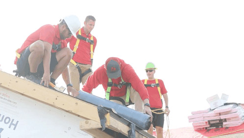 A Group Of Construction Workers Are Working On A Roof And One Of Them Is Wearing A Red Shirt With The Letter A On The Fr GIF