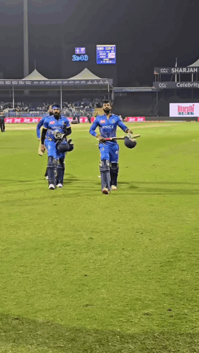 A Group Of Cricket Players Are Walking On A Field With A Scoreboard In The Background That Says Bcci GIF