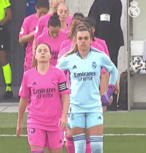 a group of female soccer players wearing pink jerseys are walking on a field .