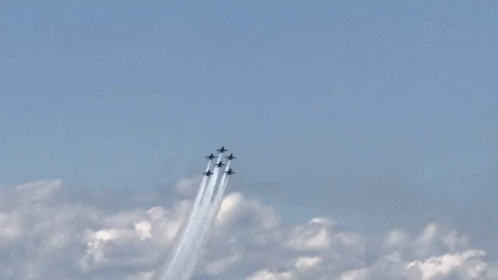 A Group Of Fighter Jets Flying Through A Blue Sky With Smoke Trails GIF