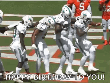 a group of football players are dancing on a field while holding a football .