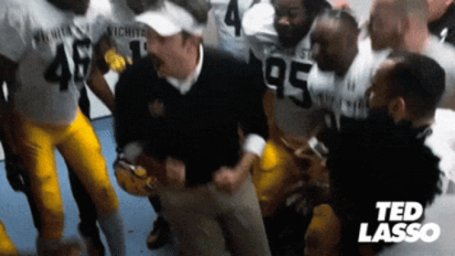 A Group Of Football Players Are Huddled Around A Man Wearing A Black Jacket With The Number 95 On It GIF