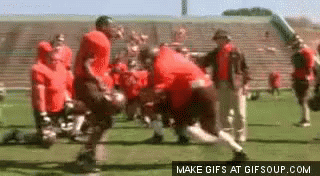 A Group Of Football Players Are Playing A Game On A Field In Front Of A Stadium . GIF
