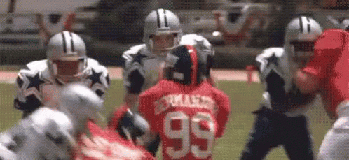 A Group Of Football Players Are Playing A Game On A Field . One Of The Players Has The Number 99 On His Jersey . GIF