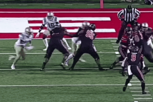 a group of football players are playing a game on a field with a referee .