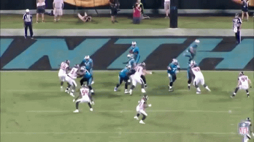 A Group Of Football Players Are Playing On A Field With A Large Nfl Logo Behind Them GIF