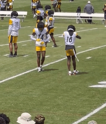 a group of football players are practicing on a field while a man in a yellow shirt watches .