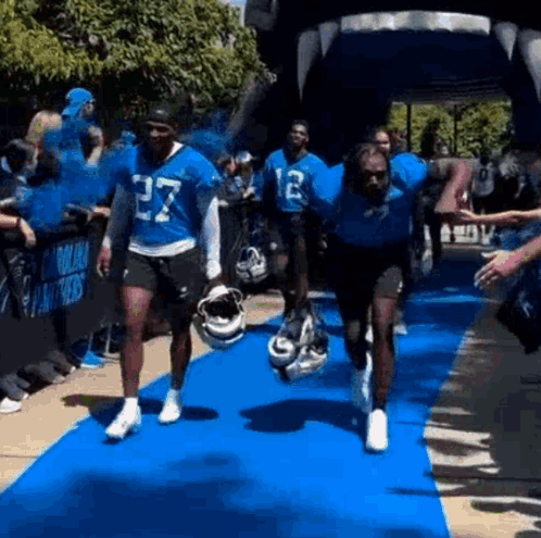A Group Of Football Players Are Running On A Blue Carpet . GIF