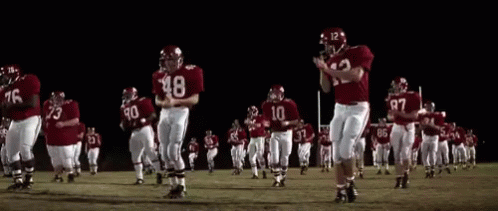 A Group Of Football Players Are Running On A Field At Night GIF