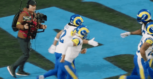 A Group Of Football Players Are Running On A Field While A Cameraman Takes A Picture Of Them . GIF