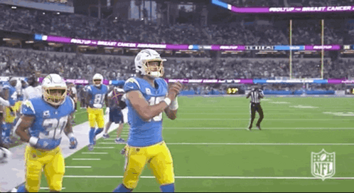 A Group Of Football Players Are Running On A Field With A Referee In The Background . GIF