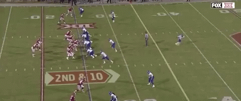A Group Of Football Players Are Running On A Field With A Referee . GIF