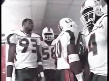 A Group Of Football Players Are Standing In A Hallway Talking To Each Other . GIF