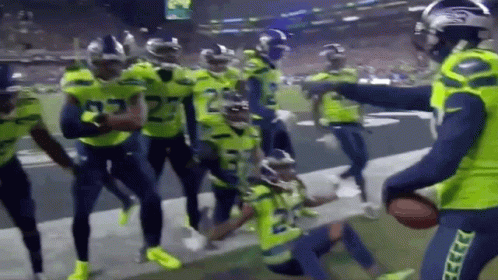 A Group Of Football Players Are Standing On A Field Holding A Ball . GIF