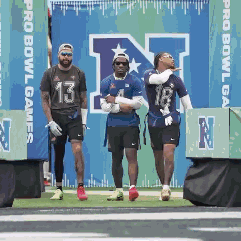 A Group Of Football Players Are Standing On A Field In Front Of A Sign That Says Pro Bowl Games GIF