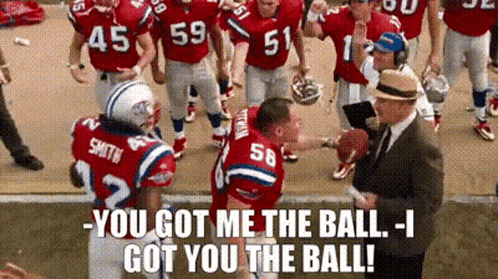 A Group Of Football Players Are Standing On A Field Talking To A Man In A Suit . GIF